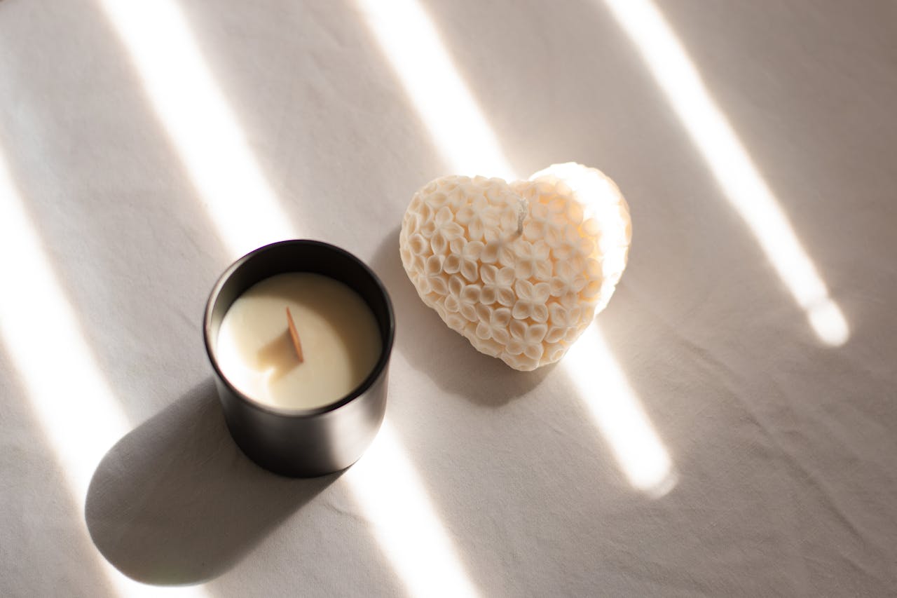 services-04 A serene tableau of a textured heart candle beside a luxury soy candle on a sunlit surface.