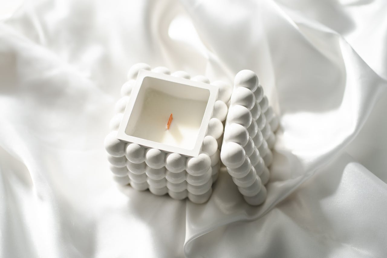 services-03 Minimalist white candle in unique cube design on satin fabric.
